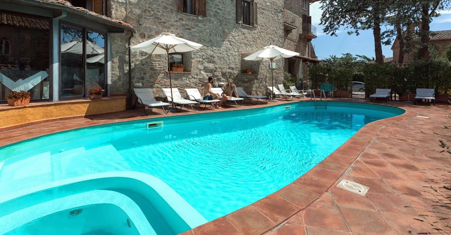 Outdoor pool beside the stone building at Relais La Fattoria